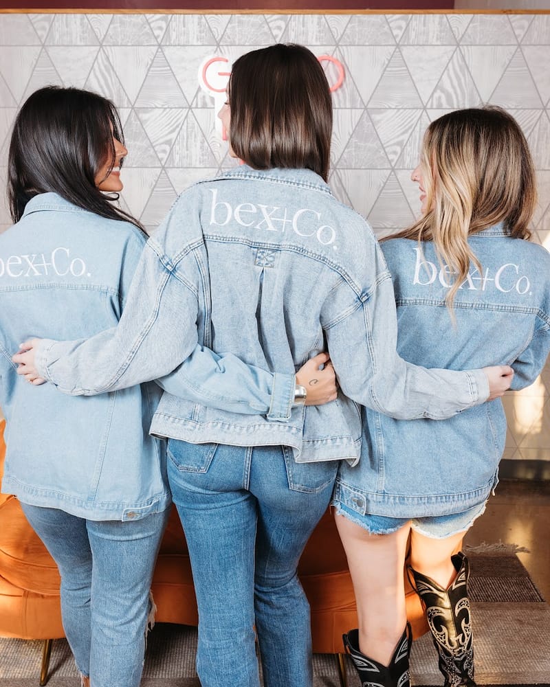 Three bex+Co. stylists in denim jackets with their arms around each other